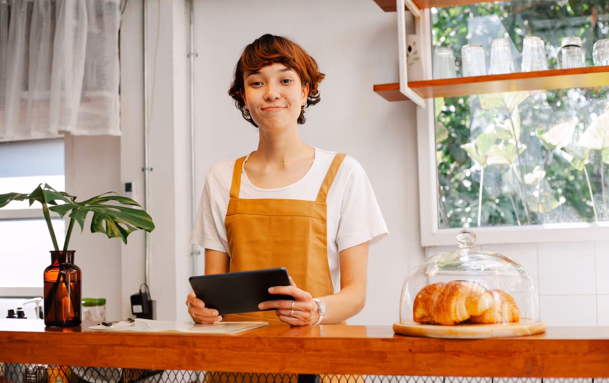 Betreiberin eines Cafés hinter dem Tresen, die ein Tablet in den Händen hält