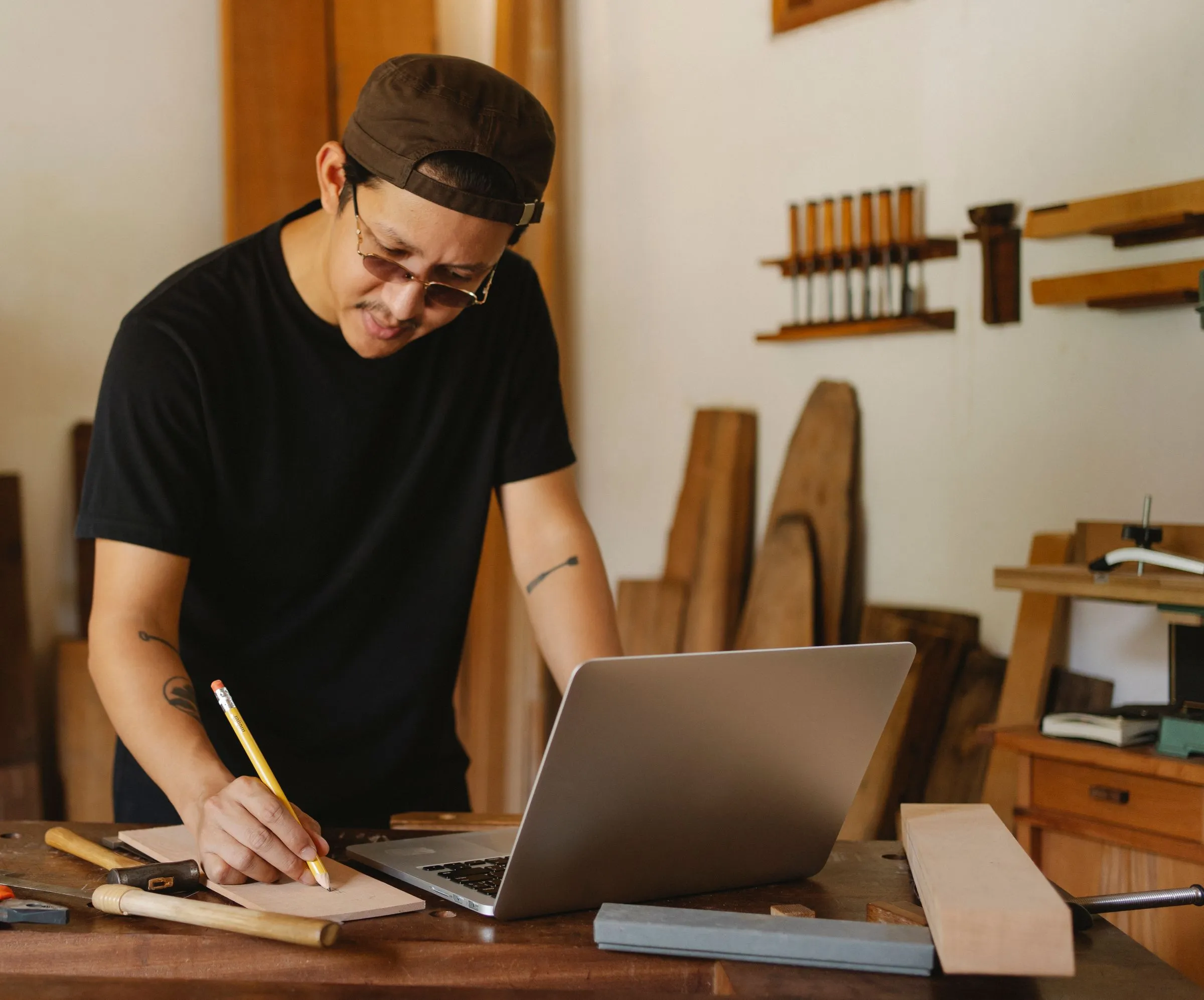Handwerker in seiner Werkstatt, der neben dem Laptop Maße auf einem Notizblock festhält