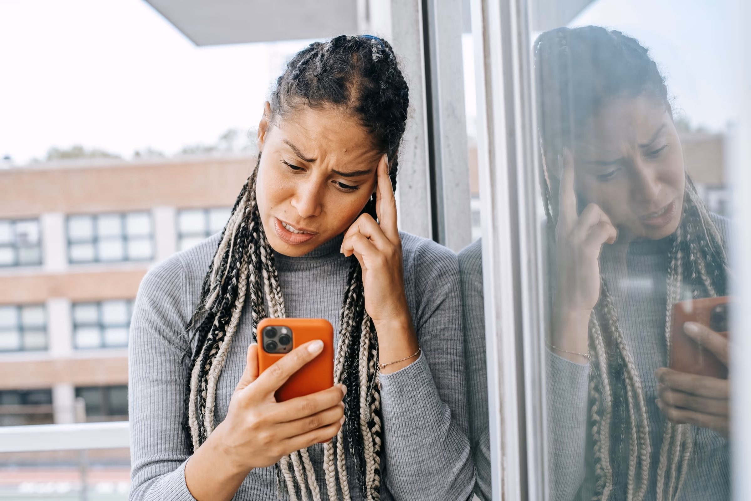 Frau, die genervt auf ihr Smartphone schaut und sich an die Stirn fasst