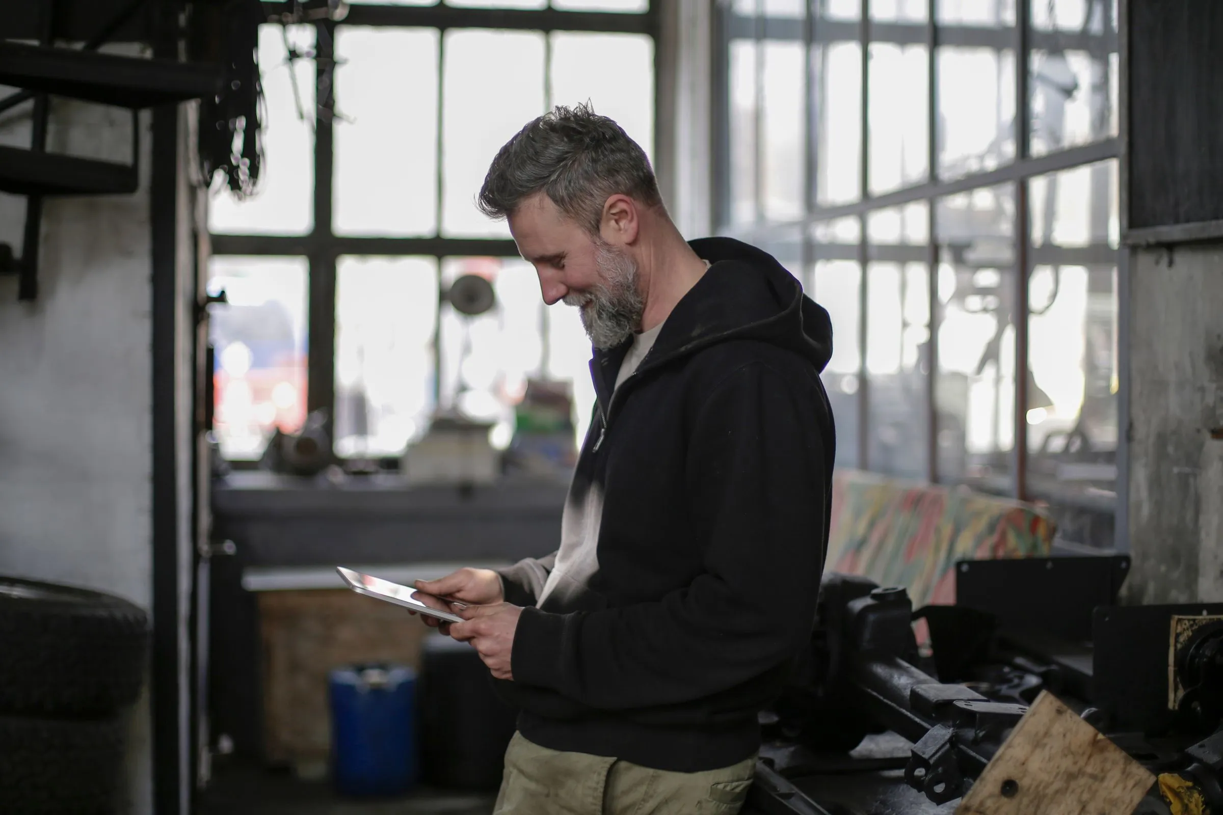 Handwerker in seiner Werkstatt, der zufrieden auf ein Tablet in seiner Hand schaut
